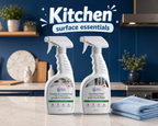 Two bottles of 'Kitchen Surface Essentials' cleaning spray on a kitchen counter with a blue wall background.
